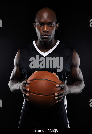 Porträt des männlichen Basketball-Spieler mit einem Ball auf schwarzem Hintergrund. Passen Sie afrikanischen Mann hält Basketball Sportbekleidung. Stockfoto