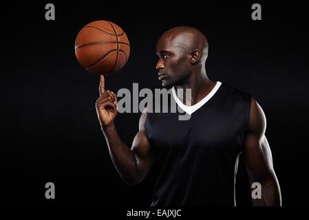 Porträt des jungen afrikanischen Athleten Ausgleich Basketball an seinem Finger auf schwarzem Hintergrund. Fokussierte Basketballspieler. Stockfoto