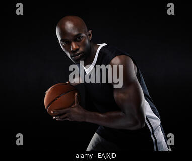 Porträt von Fit jungen männlichen Athleten Basketball zu spielen. US-amerikanischer Basketballspieler auf schwarzem Hintergrund Stockfoto