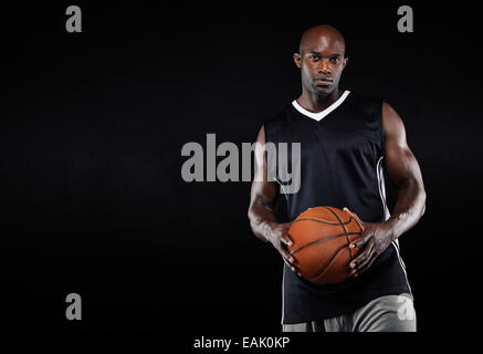 Studioaufnahme von einem jungen Basketball-Spieler stehend mit seinem Basketball. Afrikanischer Mann hält einen Basketball auf schwarzem Hintergrund Stockfoto