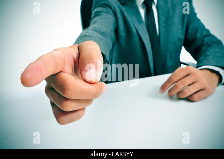 Mann trägt einen Anzug in einer Tabelle zeigt mit dem Finger den Weg nach draußen sitzen Stockfoto