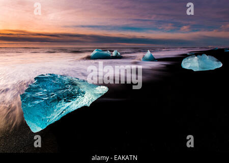 Eisbrocken auf schwarzen Lavasand Strand bei Sonnenaufgang, See Jökulsárlón, Vik, Island Stockfoto