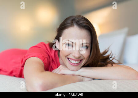 Portrait von lächelnden mittleren Erwachsenenalter Frau roten Kleid auf Bett im Schlafzimmer Stockfoto