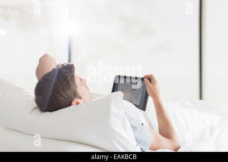 Junger Mann auf dem Bett liegend und mit tablet Stockfoto