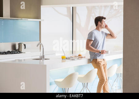 Mann mit Kaffeetasse mit Telefon in moderne Küche Stockfoto