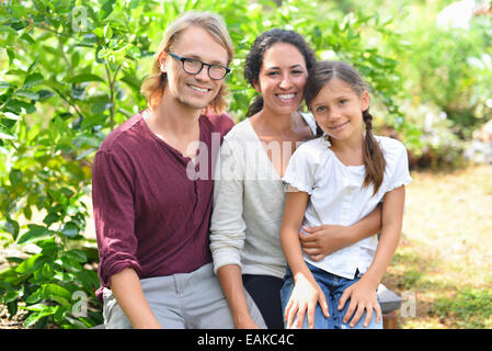 Porträt von lächelnden Eltern mit Tochter sitzt auf der Bank im Garten Stockfoto