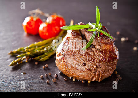Stück rotes Fleisch Steak mit Gemüse und Kräutern, serviert auf schwarzem Steinoberfläche. Stockfoto