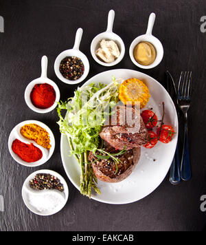 Stück rotes Fleisch Steak mit Gemüse, Kräutern und Gewürzen, serviert auf schwarzem Steinoberfläche. Schuss aus Draufsicht Stockfoto