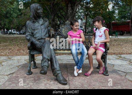 Zwei Mädchen sitzen auf einer Bank neben einer Bronze-Skulptur von John Lennon, Havanna, Kuba Stockfoto