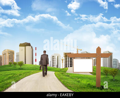 Geschäftsmann geht auf die Straße. Sicht nach hinten. Gebäude, Wiese, hölzernen Schild und Himmel im Hintergrund Stockfoto
