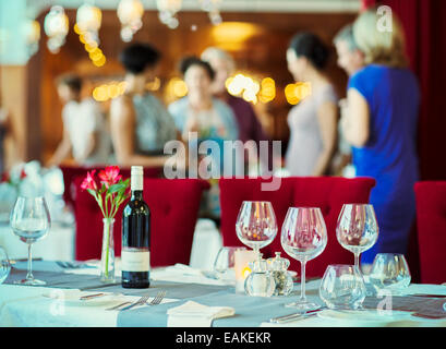 Weingläser und Flasche Rotwein am Tisch im Restaurant, Menschen im Hintergrund Stockfoto