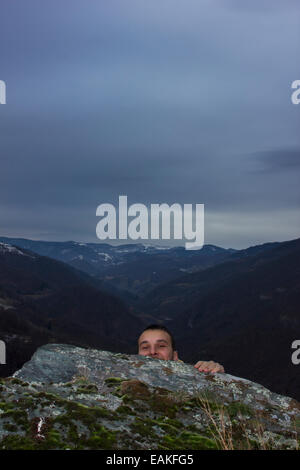 Wanderer, versteckt sich hinter den Rand der Klippe mit dem Tal im Hintergrund Stockfoto