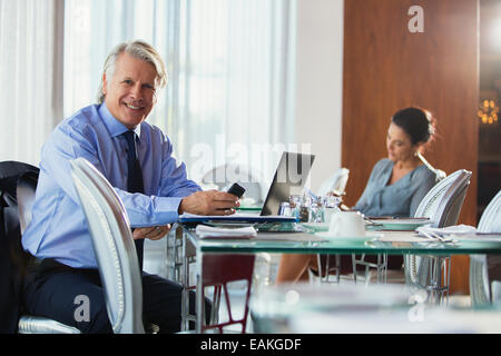 Porträt von lächelnden reifer Geschäftsmann mit Smartphone und Laptop im restaurant Stockfoto