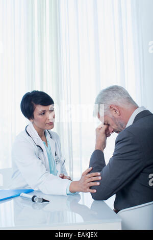 Ärztin am Schreibtisch sitzen und tröstet traurigen patient Stockfoto