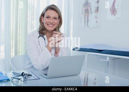 Porträt von lächelnden Ärztin mit Laptop im Büro am Schreibtisch sitzen Stockfoto