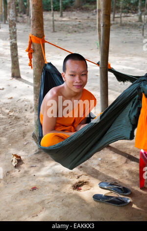 Junger vietnamesischer Mönch im Khmer-Theravada-buddhistischen Kloster in Tra Vinh entspannt in einer Hängematte mit seinem Handy. Stockfoto