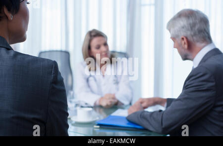 Ärztin, Mann und Frau im Gespräch am Tisch im Konferenzraum Stockfoto