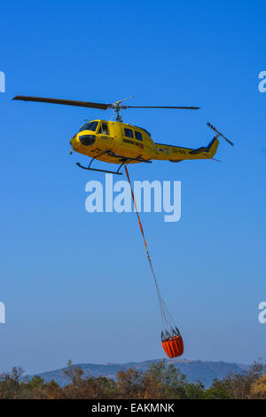 Hubschrauber mit einem Eimer voller Wasser zur Brandbekämpfung Stockfoto