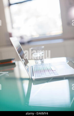 Offenen Laptop und ein Glas Wasser auf Glasschreibtisch im Büro Stockfoto