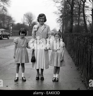 1950er Jahre, historisches Bild einer Mutter, die auf einem Straßenpflaster mit ihren beiden kleinen Kindern, kleinen Mädchen in Kleidern, auf dem Weg zur sonntagsschule in Manchester, England steht, eine traditionelle Stadt in Großbritannien zu dieser Zeit, vor allem in Nordirland. Stockfoto