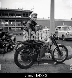 1950er Jahre, ein Mann, der eine Bikerjacke und wellington-Stiefel trägt, sitzt draußen auf seinem Triumph-Motorrad, das ein verkratztes union-Jack-Emblem auf dem Benzintank trägt, England, Großbritannien. Stockfoto