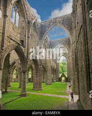 Spektakuläre Reste der 12. Jahrhundert Tintern Abbey mit 2 Personen in den Schatten gestellt durch seine riesigen Mauern und Bögen, die in blauen Himmel steigen Stockfoto