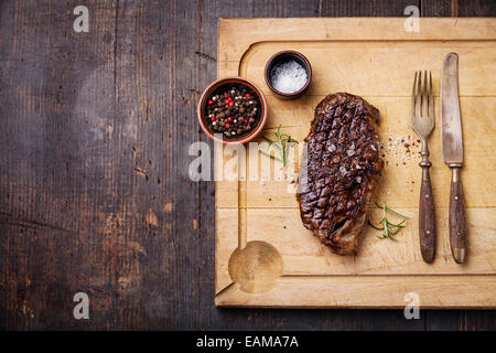 Gegrilltes New York Striploin Steak mit Salz und Pfeffer auf Fleisch Schneidbrett auf dunklem Holz Stockfoto