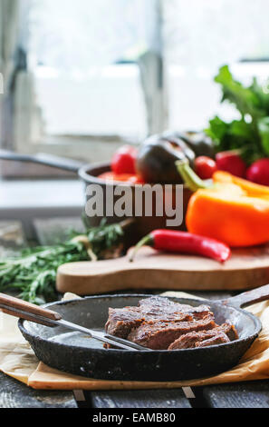 Gegrilltes Steak in Vintage-Pfanne mit frischem Gemüse auf alten Tisch in der Nähe von Fenster im Tageslicht Stockfoto