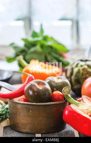 Variation von frischem Gemüse Tomaten, Pfeffer, Paprika, Artischocken und Brüssel Sprossen auf alten Tisch in der Nähe von Fenster im Tageslicht. Stockfoto