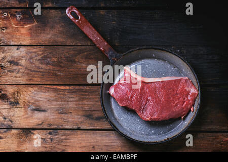 Rohes Steak in Vintagev Pfanne bei alten Holztisch. Ansicht von oben. Stockfoto