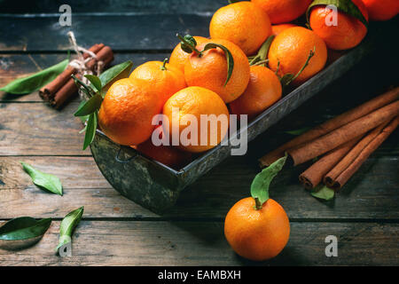 Mandarinen mit Blättern und Zimtstange auf alten Holztisch. Stockfoto