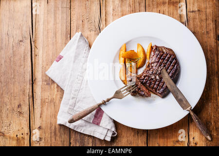 Gegrillte südamerikanischen Premium-Rindfleisch New York Steak mit gebratene Kartoffelspalten auf weißen Teller auf hölzernen Hintergrund Stockfoto