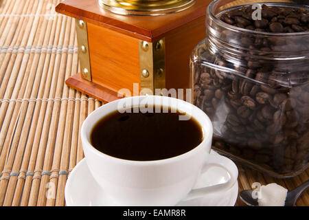 Tasse Kaffee, Topf voller Bohnen und Mühle auf Stroh Stockfoto