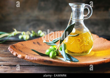 Eine Flasche Olivenöl mit Ölzweig in Handarbeit Ton Platte über Holztisch. Stockfoto