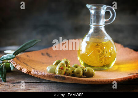 Grüne Oliven und Flasche Olivenöl in Handarbeit Ton Platte über Holztisch serviert. Stockfoto