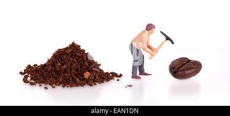 Miniatur-Arbeiter mit Spitzhacke arbeitet an einer Kaffeebohne Stockfoto