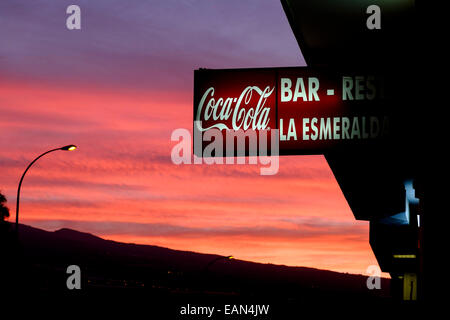 Roter Himmel im Morgengrauen mit Coca Cola Schild an der Bar La Esmeralda, Playa San Juan, Teneriffa, Kanarische Inseln, Spanien. Stockfoto