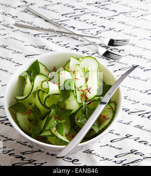 Gurkensalat mit dekorativen Schnitt in einer dunklen Platte auf eine weiße Tischdecke mit einem dekorativen silbernen Messer und Gabeln zu schreiben Stockfoto