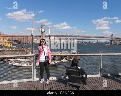 Junge Frau, die die Selfie mit Stick mit Brooklyn Bridge im Hintergrund Manhattan, New York, USA Stockfoto