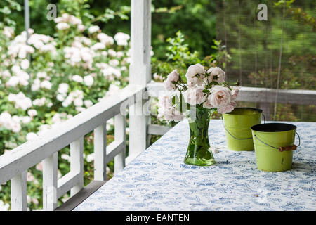 Vase mit frischen Frühling rosa Rosen sitzt am Tisch mit floral Tischdecke mit Citronella Kerzen auf eine alte Mode-Portal Stockfoto