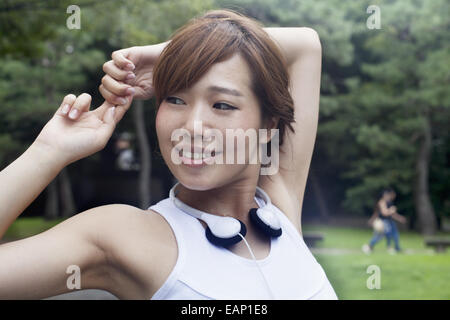 Eine Frau in einem Kyoto-Park tragen von Kopfhörern. Jogging Set tragen und stretching vor dem Training. Stockfoto