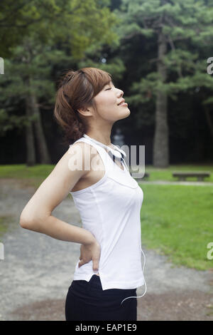 Eine Frau in einem Kyoto-Park tragen von Kopfhörern. Jogging Set tragen und stretching vor dem Training. Stockfoto