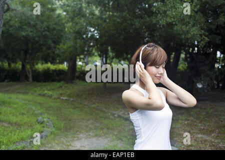 Eine Frau in einem Kyoto-Park tragen von Kopfhörern. Jogging Set tragen. Stockfoto