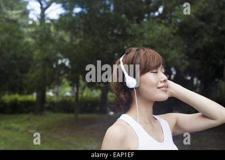 Eine Frau in einem Kyoto-Park tragen von Kopfhörern. Jogging Set tragen. Stockfoto