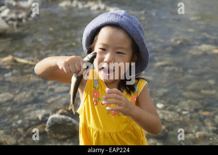 Junges Mädchen mit einem Sommerhut, der einen Fisch hält. Stockfoto