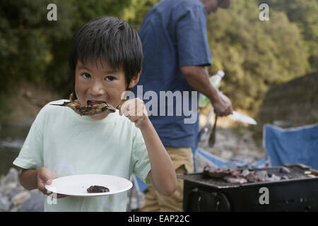 Kleiner Junge einen gegrillten Fisch zu essen, bei einem Picknick. Stockfoto