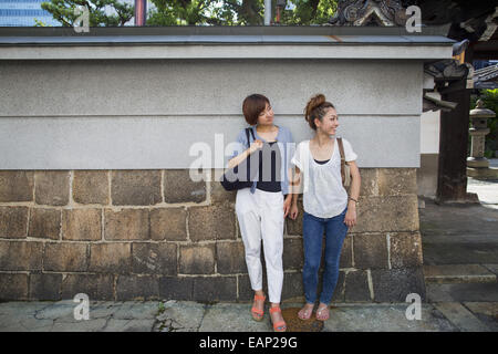 Zwei Frauen stehen im Freien, an eine Wand gelehnt. Stockfoto