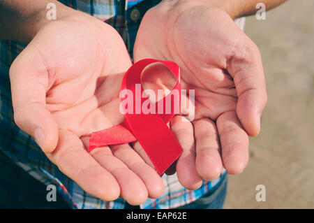 junger Mann mit einer roten Schleife für den Kampf gegen AIDS in seinen Händen, mit einem Filtereffekt Stockfoto