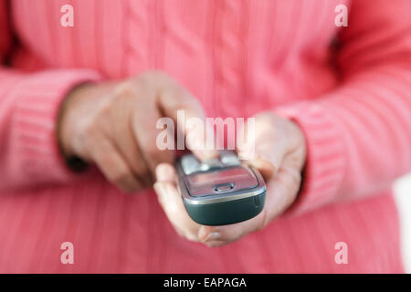 Eine rechtshändige ältere Frau, die eine Handtastatur mit einem Touch Phone verwendet, um eine Telefonnummer zu wählen, um von zu Hause aus einen Anruf zu tätigen. England, Großbritannien, Großbritannien Stockfoto