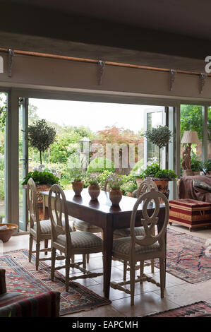 Rundheck hölzerne Stühle um antike Bauernhaus Tisch im Speisesaal mit Fenstertüren zum Garten öffnen Stockfoto